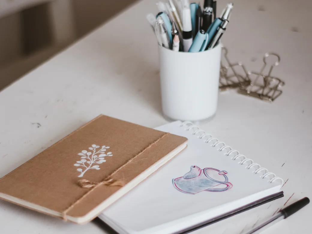 Papel, un cuaderno kraft y un vaso con lápices sobre un escritorio